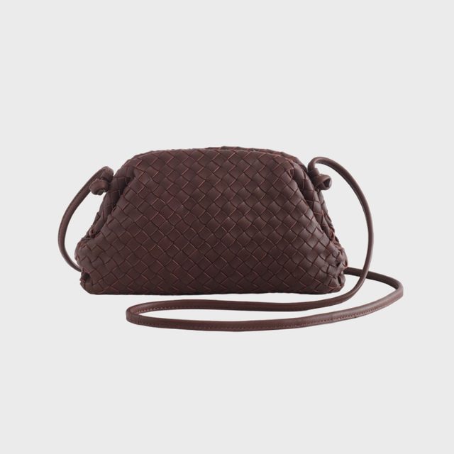 Woven brown handbag rests with a long strap, displayed against a plain white background.