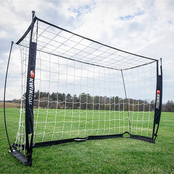 Soccer goal stands on green grass field under a cloudy sky. The net is attached to a sturdy frame. Text: 