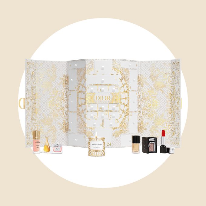 An ornate advent calendar displays small Dior beauty products, including perfumes, a candle, and cosmetics, set against an intricate gold and white design.