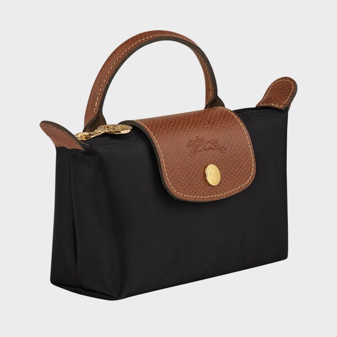 A black handbag with a brown leather flap and handle, features a gold button, set against a plain gray background.
