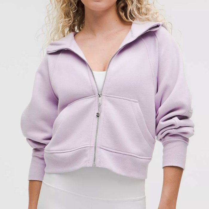 A person wears a light purple zip-up hoodie with white leggings, standing against a plain background.