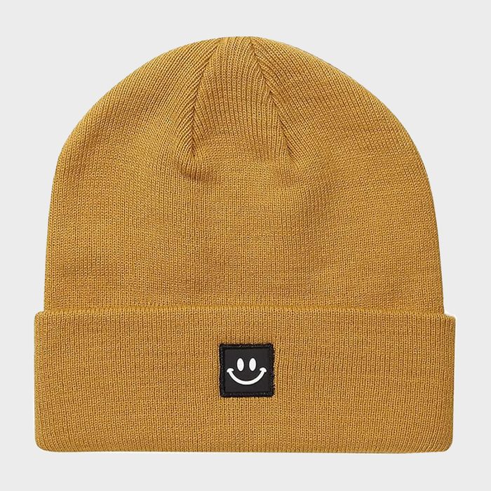 Yellow beanie resting flat, featuring a stitched black patch with a white smiley face, against a plain white background.