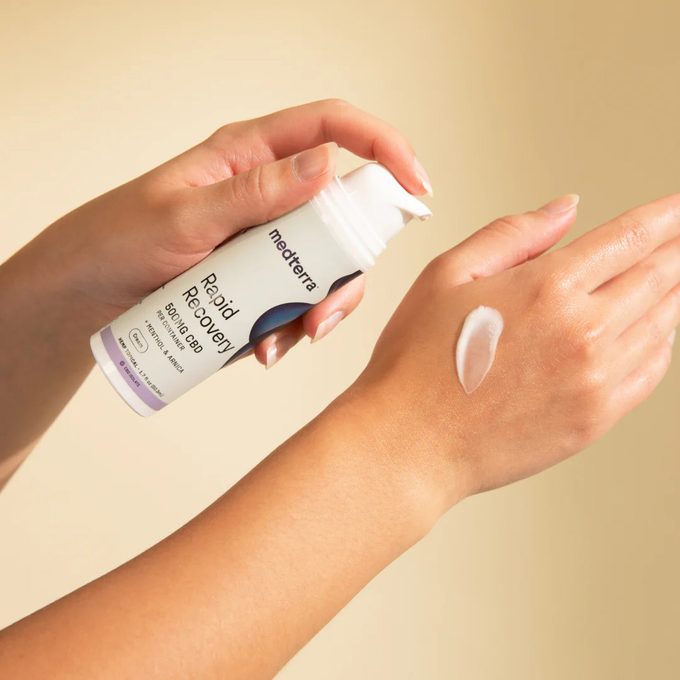 Hand applies Medterra Rapid Recovery cream onto the other hand, against a neutral background.