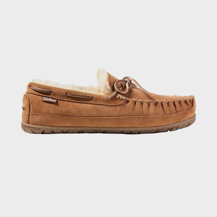 Brown moccasin slipper sits on a white background, featuring leather laces and a plush, shearling-lined interior.