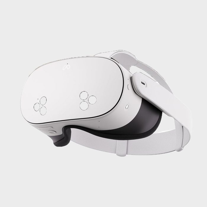 A white VR headset rests against a neutral gray background, with adjustable straps and circular sensors on the front, designed for immersive experiences.