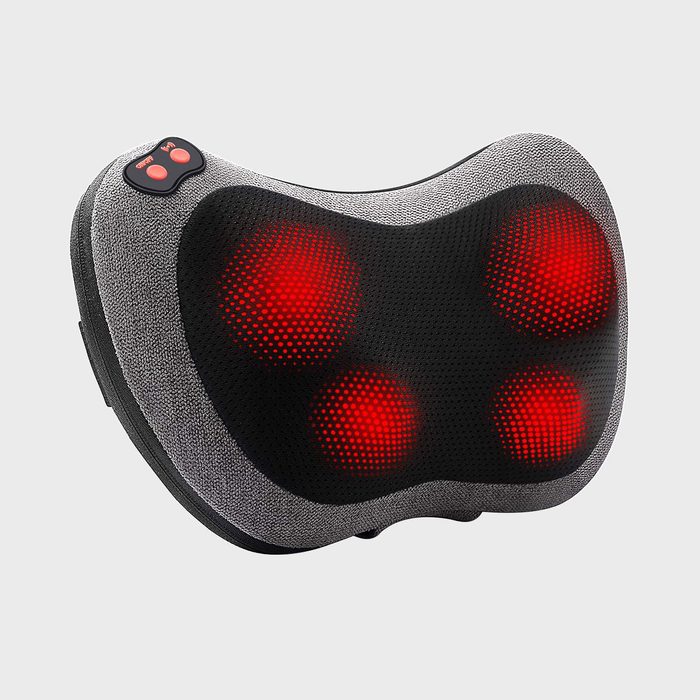 A massage cushion emits red light, suggesting heat function, resting in a minimalist, light gray setting.