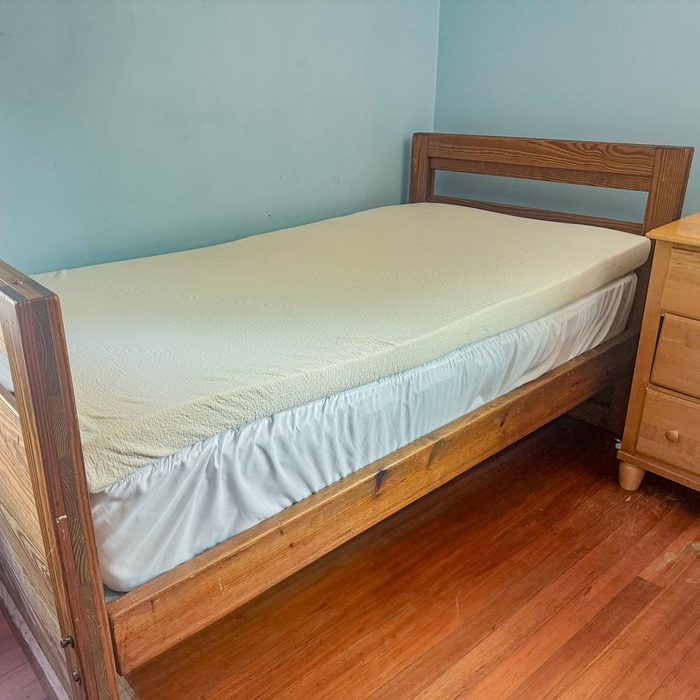 Bed with wooden frame sits against a light blue wall, adjacent to a wooden nightstand on a hardwood floor.