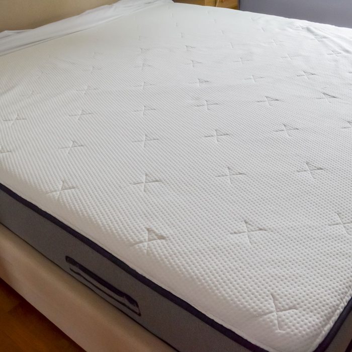 A white mattress with quilted texture lies on a bed frame in a bedroom.