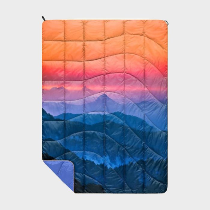 Quilt displays a colorful gradient, transitioning from warm orange to cool blue, depicting a scenic mountain range, set against a plain white background.