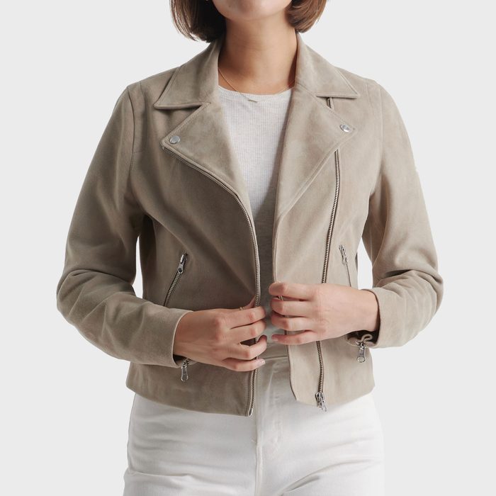 Person adjusts a beige suede jacket while standing, against a plain white background.