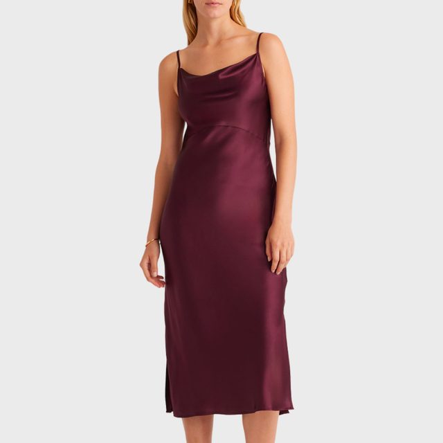 Woman wearing a sleeveless, burgundy satin slip dress, standing against a plain white background.