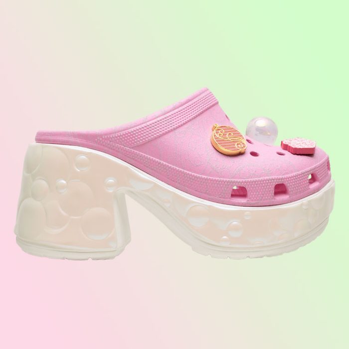 Pink platform clog adorned with charms sits against a soft, gradient background of pink and green hues.
