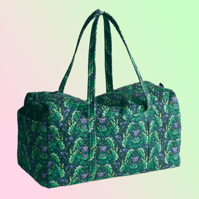 A quilted duffle bag rests upright, showcasing a green floral pattern, set against a gradient pink and green background.