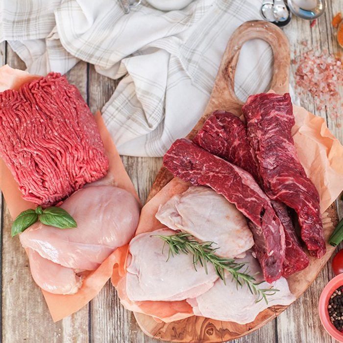 Various raw meats arranged on parchment with herbs, displayed on a wooden board and rustic table, alongside a cloth and spices.