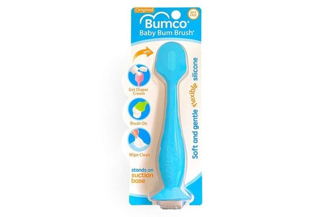 Blue silicone brush stands upright on packaging, designed for applying diaper cream. Circular icons demonstrate application steps: get diaper cream, brush on, wipe clean.