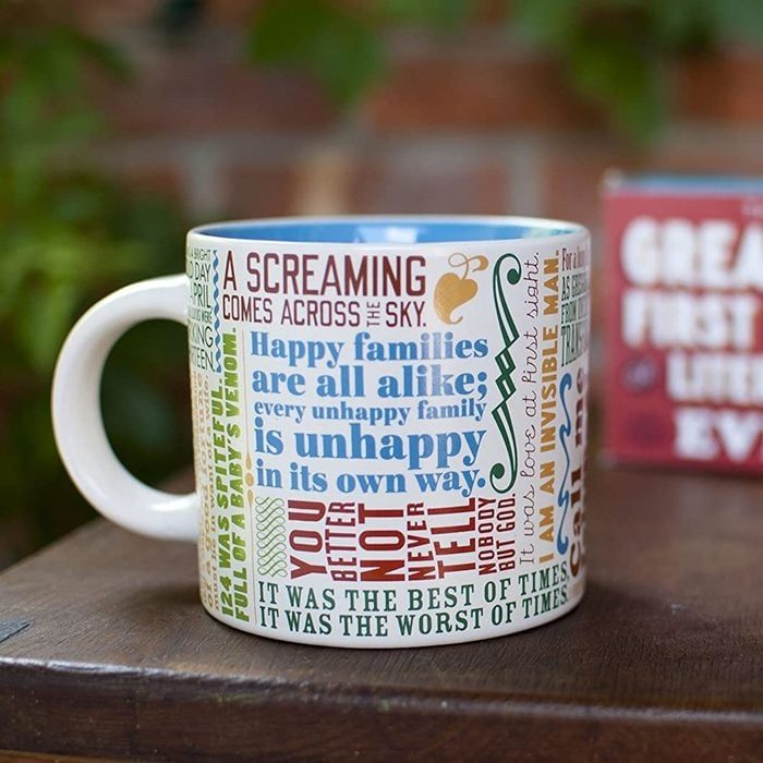 Mug displays colorful text quotes, resting on a wooden surface, with a blurred brick background.