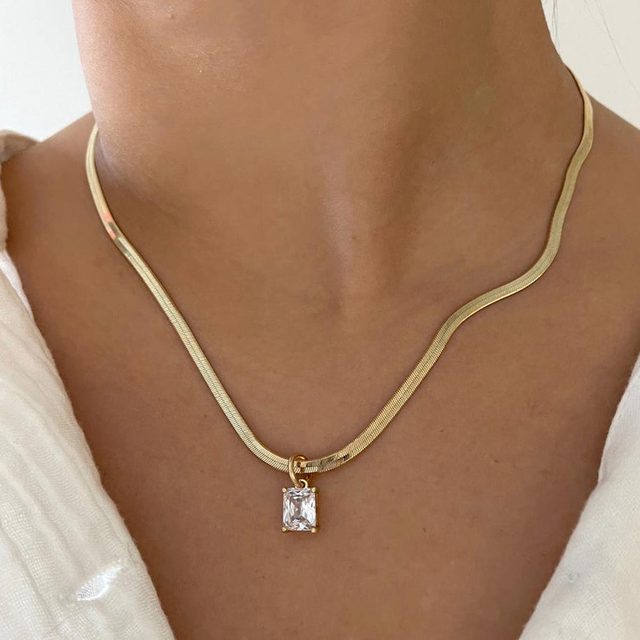 Necklace displays a rectangular pendant, worn around a person's neck, against a light fabric background.
