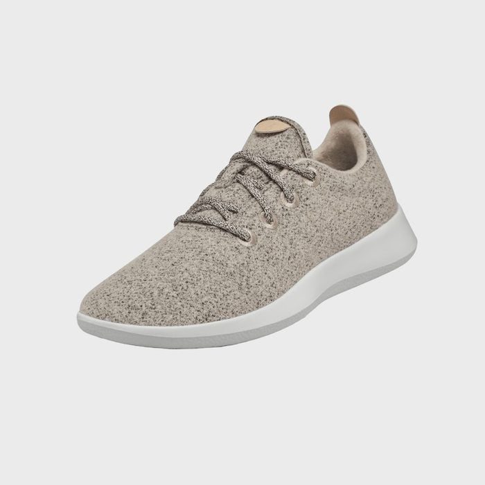 A beige sneaker with laces sits against a plain gray background, showcasing a knitted texture and white sole.