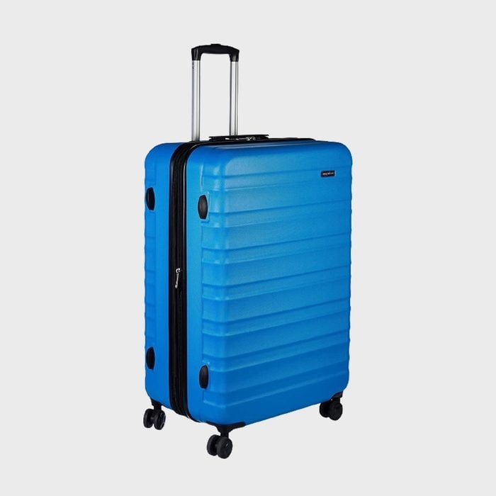 Blue suitcase stands upright, featuring four wheels and a retractable handle, set against a plain gray background.