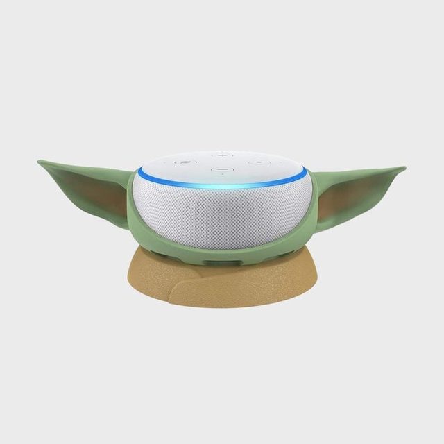 A smart speaker resembling a character with green ears rests on a brown base, set against a plain, light gray background.