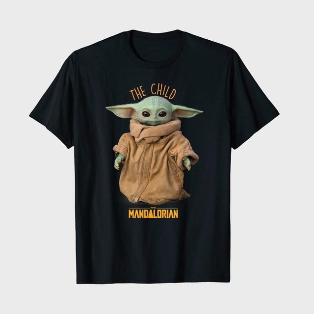 T-shirt displays a small green creature wearing a beige coat with text 