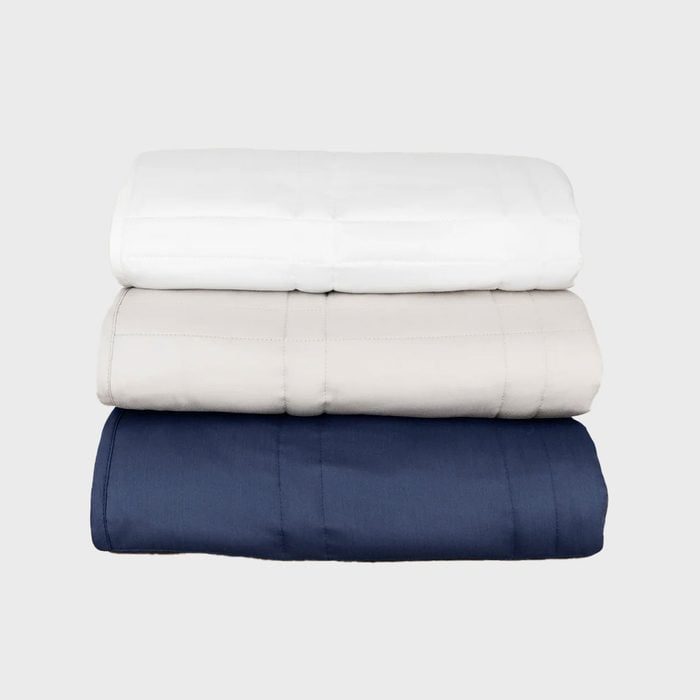 Three neatly folded blankets, stacked in white, beige, and navy, on a plain light gray background.