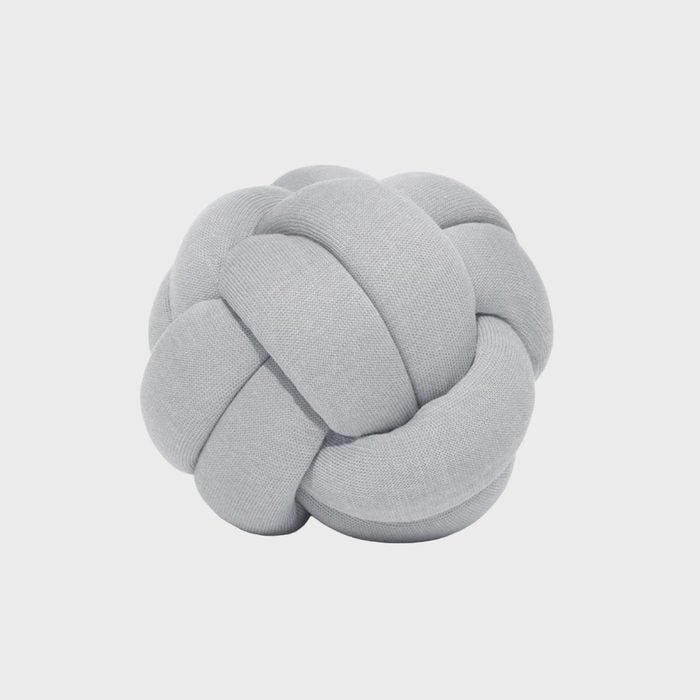 A soft, grey knot pillow sits against a plain white background, showcasing intricate loops and a plush texture.