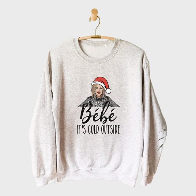 Sweatshirt hangs on a hook, featuring a woman in a Santa hat above the text 