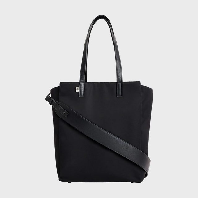 A black tote bag with dual handles and a crossbody strap, featuring a small logo tag, set against a white background.