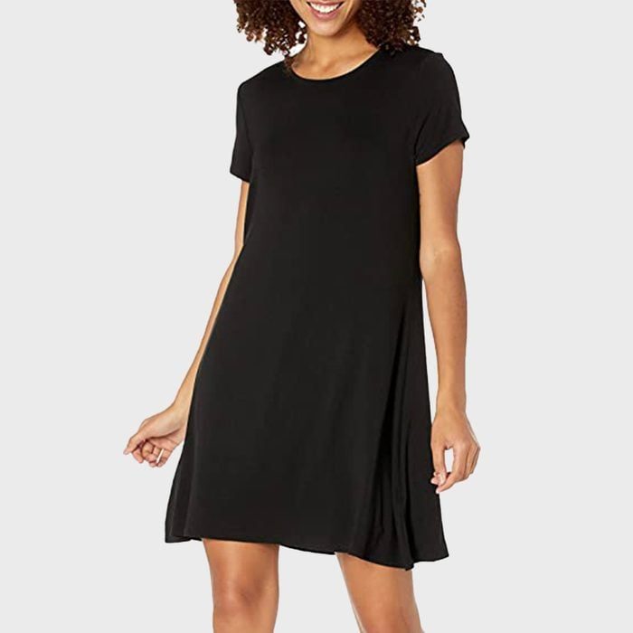 A person wears a black, short-sleeved dress while smiling, set against a plain white background.