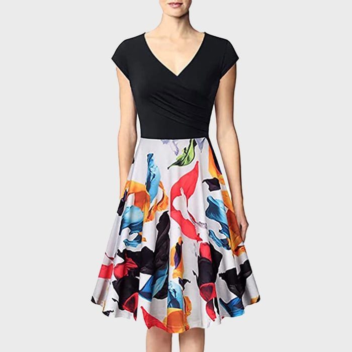 A woman models a dress with a black top and a colorful, abstract-patterned skirt, set against a plain gray background.