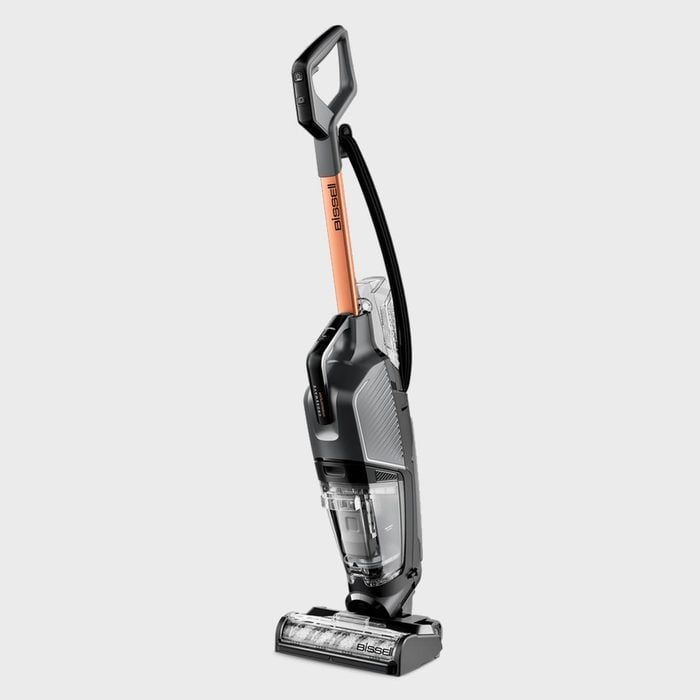 Upright vacuum cleaner standing on a grey background, featuring a transparent dustbin and orange handle labeled 