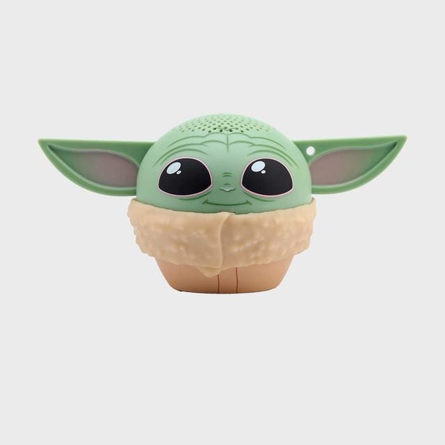 A small, green, baby alien-themed speaker sits against a plain, light gray background.
