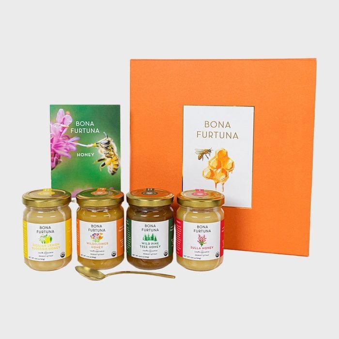 Jars of honey are arranged with a gold spoon and colorful packages; backdrop includes an orange box labeled 