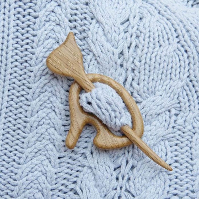 Wooden shawl pin secures knit fabric, featuring light blue cable-knit pattern.
