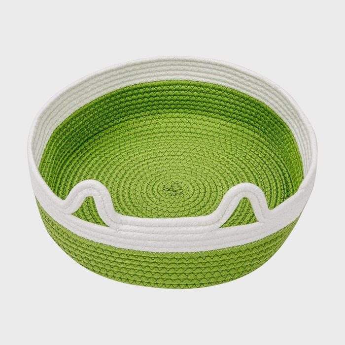 A green and white woven basket rests empty against a plain, neutral background.