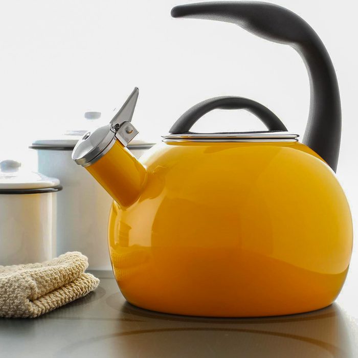 Yellow teapot sits on a counter; white pots and a folded beige cloth are nearby, enhancing a kitchen setting.