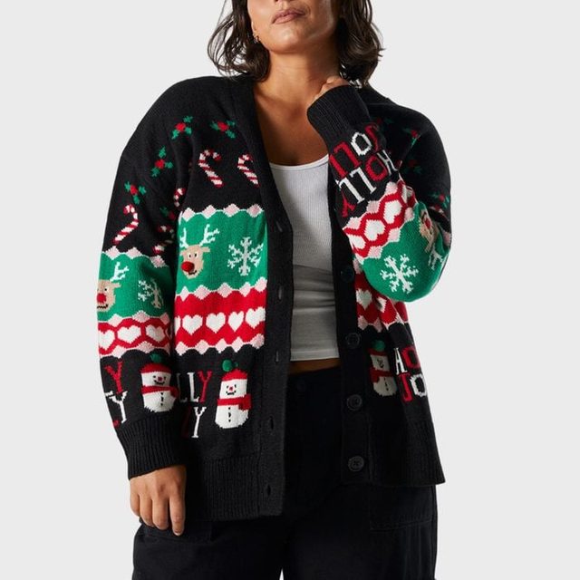 Cardigan with colorful Christmas patterns and text â€œHOLLY JOLLY,â€ worn by a person in a white top, standing against a plain background.