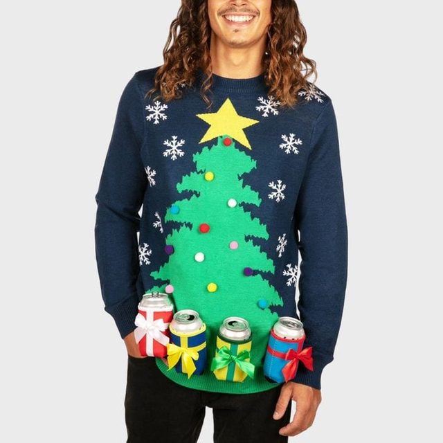 Sweater displays a decorated Christmas tree with snowflakes; four beverage can holders attached below, each wrapped with colorful ribbons. Man standing against a plain background.