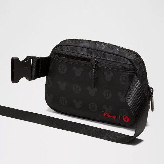 A black crossbody bag features a zipper and printed logos, set against a neutral background. Text: 