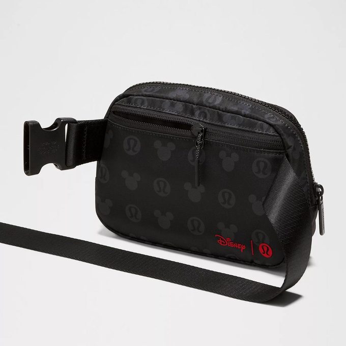 A black crossbody bag features a zipper and printed logos, set against a neutral background. Text: 