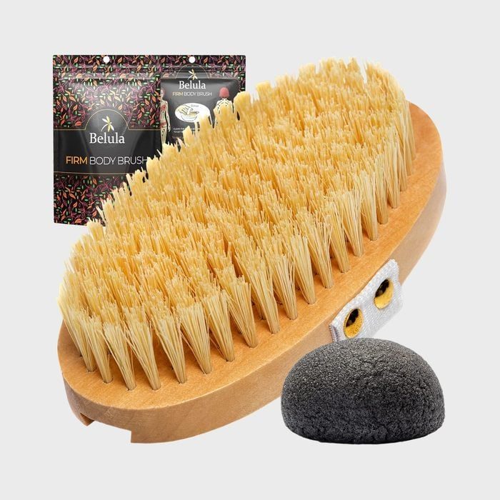 Oval body brush with firm bristles sits beside a pumice stone; packaging labeled 