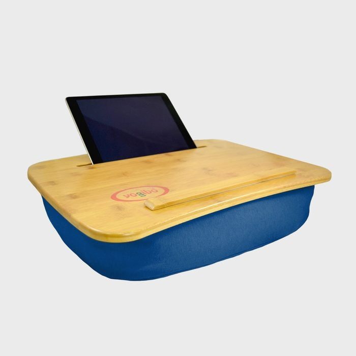 Lap desk holds tablet upright on a wooden surface with a cushioned base, in a minimalistic setting. 