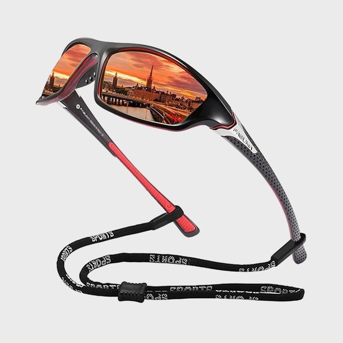 Sunglasses reflect a vibrant cityscape during sunset, featuring buildings and a river. The frame is black with red accents, accompanied by a black sports strap.