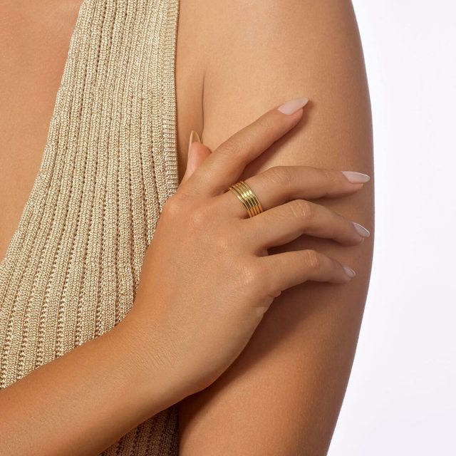 Hand wearing a gold ring rests on an arm, with a textured beige fabric in the background.
