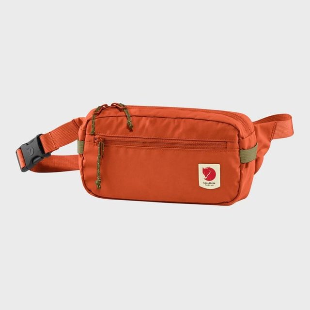 The orange waist bag rests on a plain background, featuring a front zipper and a logo with a fox emblem at the lower right.
