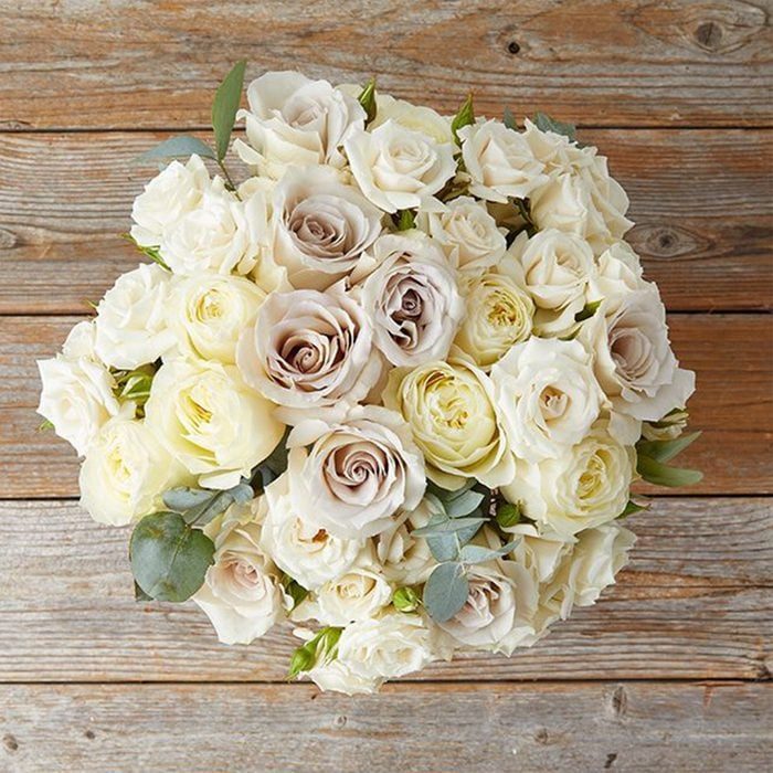 A bouquet of white and cream roses rests on a wooden surface, creating a rustic, elegant display.