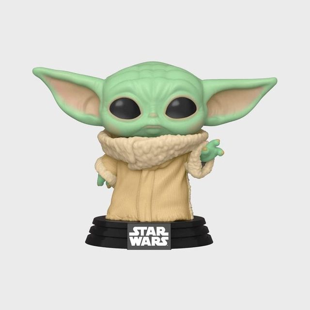 A small green figurine holds out one hand, wearing a beige coat, standing on a black base labeled 