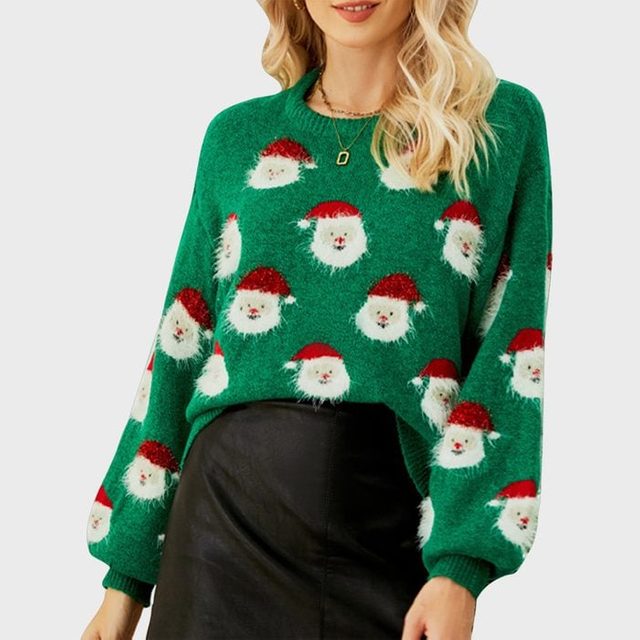 Woman wears a green sweater patterned with Santa faces, paired with a black skirt, standing against a plain gray background.
