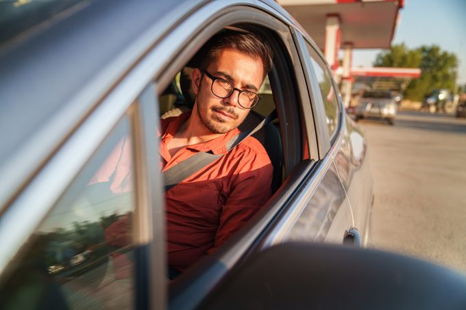Man is at the gas station in the car looking in his side view mirror